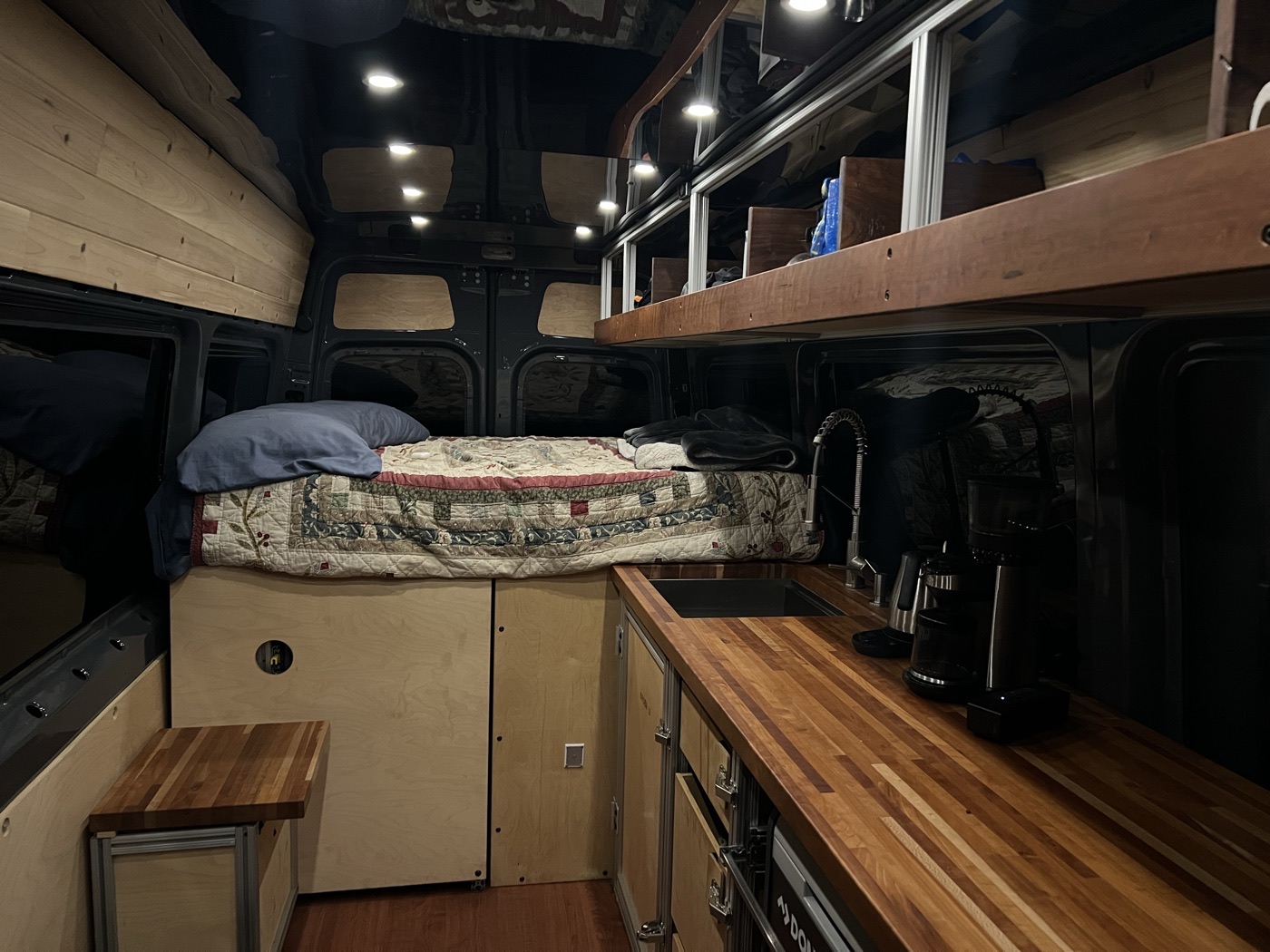 Ender 1.0 interior at night — sleeping platform, butcher block counter, coffee maker, and recessed lighting
