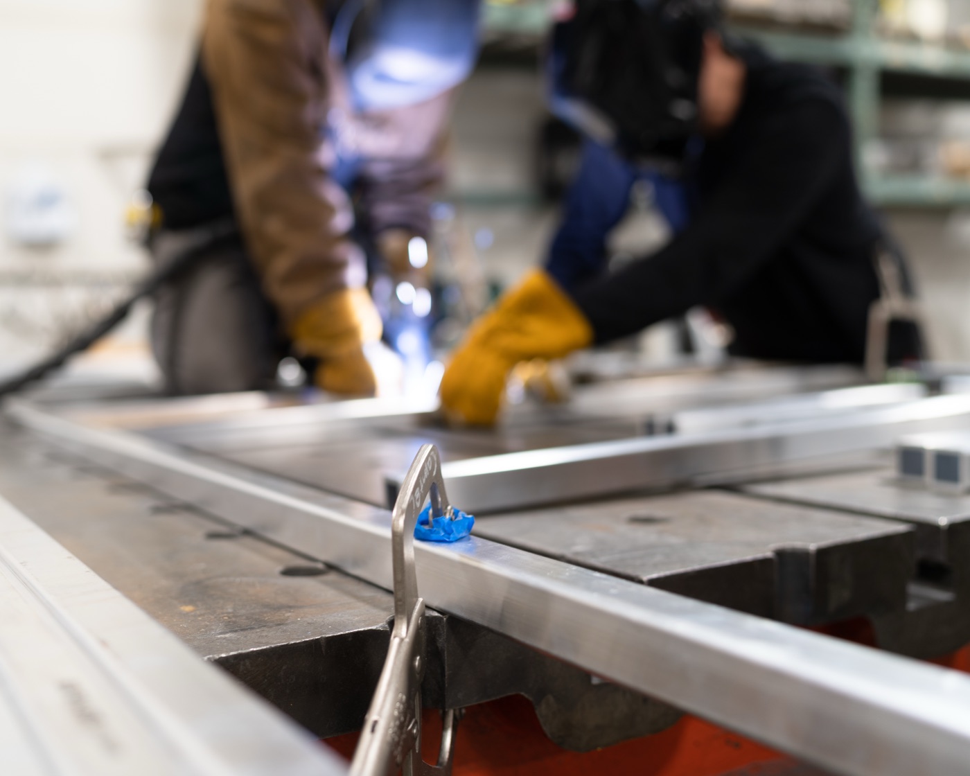 Low-angle view of aluminum frame with TIG welding arc glowing in background
