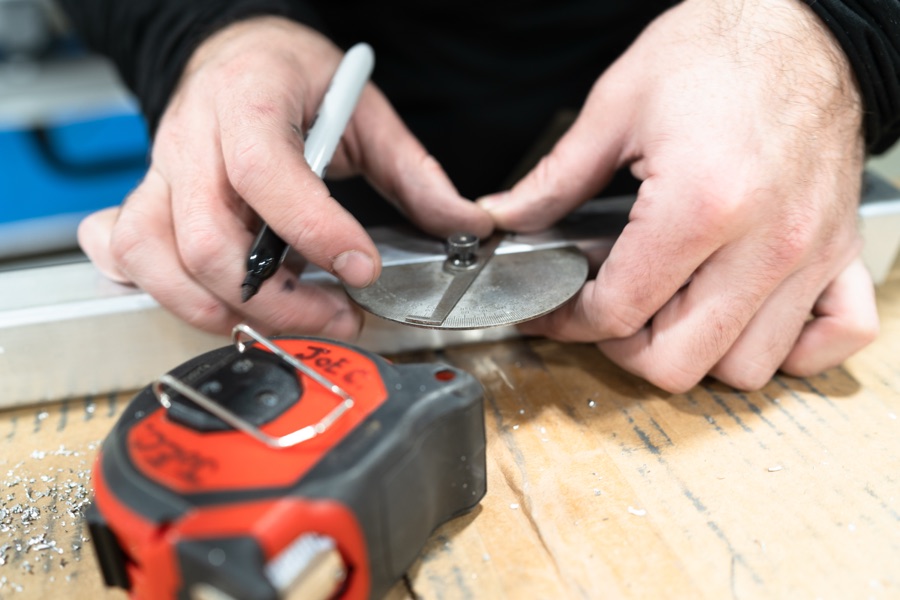 Hands precisely marking a metal component with tape measure and marker