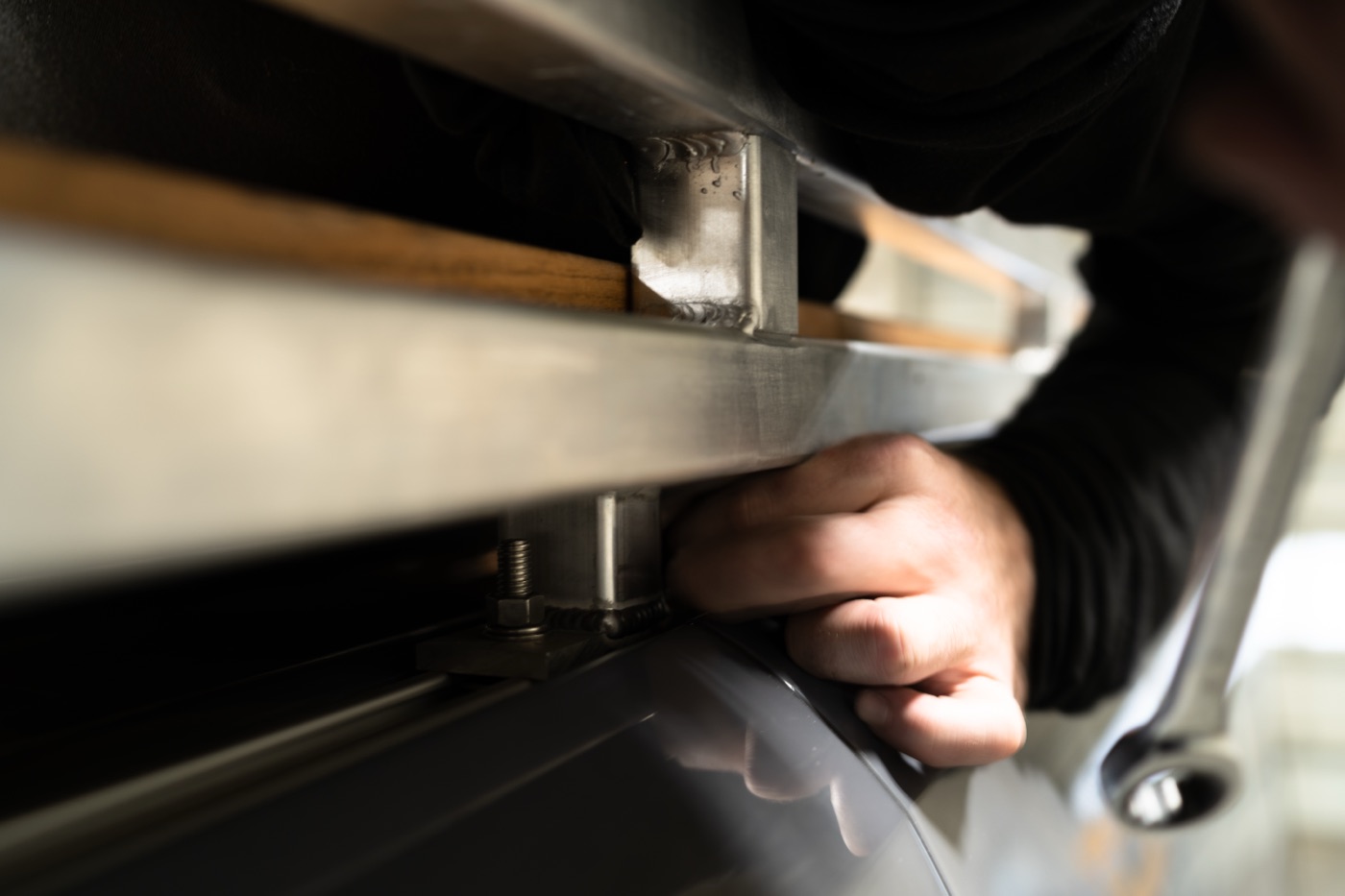 Hands fastening the roof rack to the Sprinter's roof rail with stainless hardware