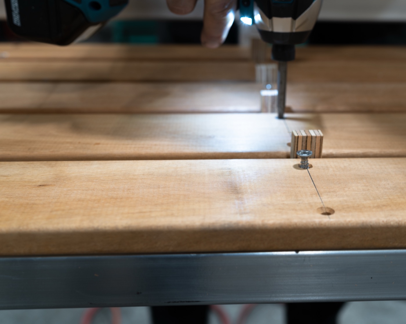 Driving a stainless steel screw through a Tigerwood slat into the aluminum frame, wooden spacer blocks holding the gap